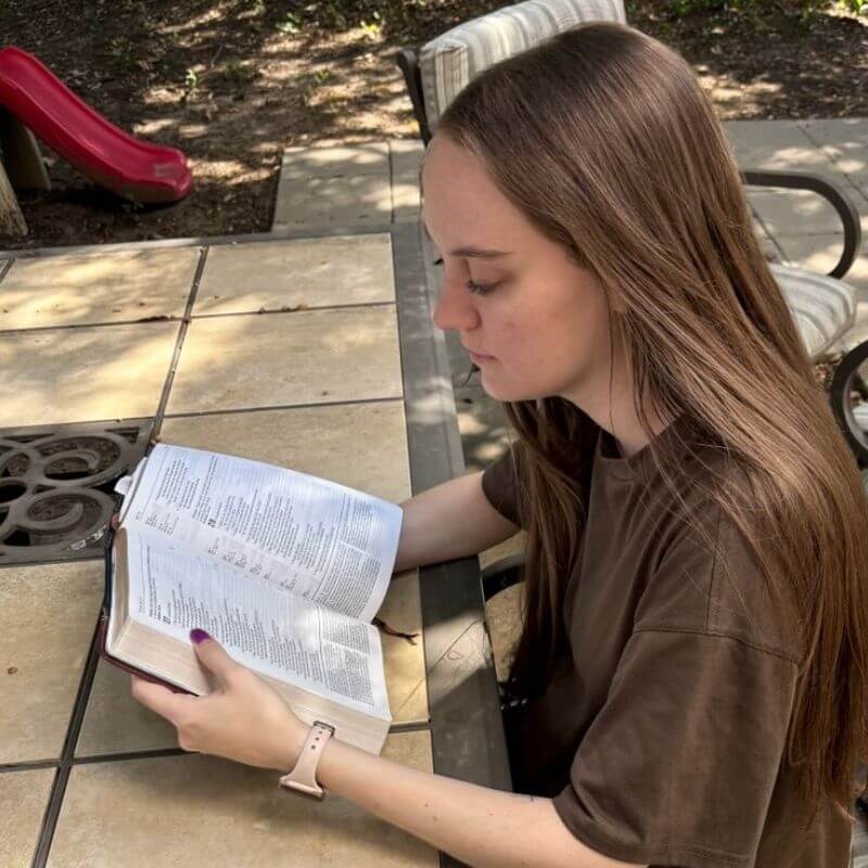 Woman in brown shirt reading Bible outside